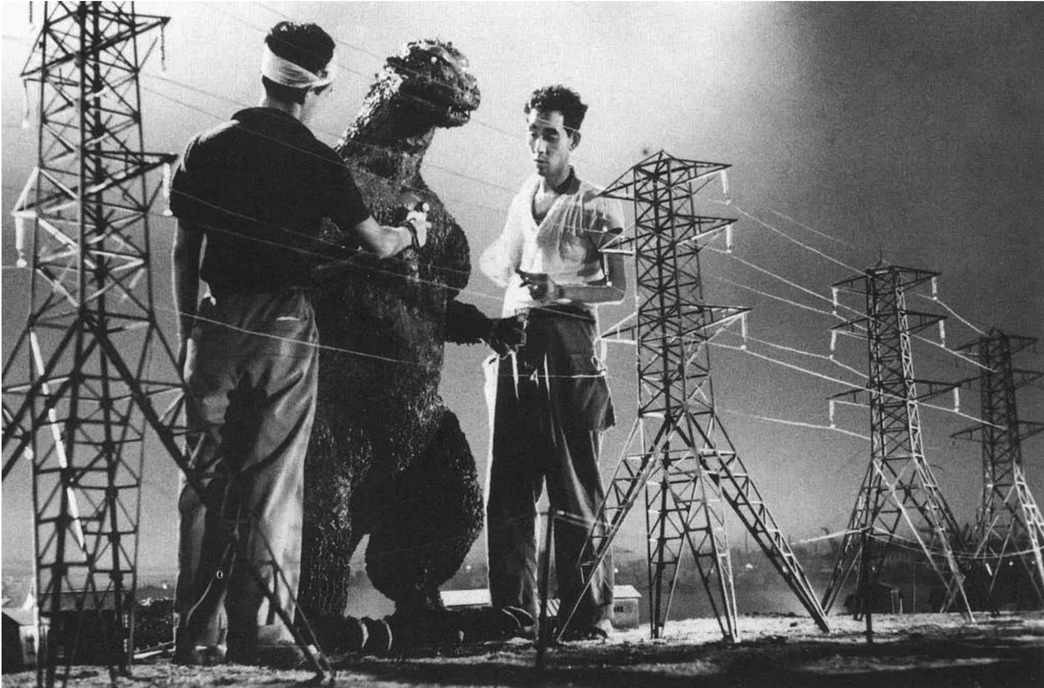 Behind the scenes on Gojira (1954): two crew members standing with the suited monster among model power pylons.
